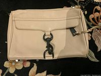 Front side of Rebecca Minkoff leather purse showing beige leather with black hardware clasp and chain strap on a dark floral background.