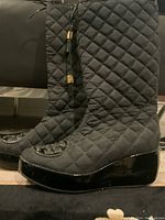 Side view of the black quilted fabric Tory Burch boots with patent leather wedge heel and toe cap showing the full boot profile and quilted pattern.