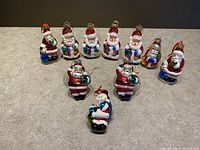 Photo of all ten Santa glass Christmas tree decorations arranged on a beige surface showing variety of designs and colors.