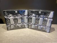 Two sealed packages of Tom Smith Christmas crackers, each with six crackers visible through plastic packaging, with black, white, and silver festive design.