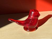 Red glass cardinal bird paperweight displayed on light wood surface with red wall background showing the form, texture, and color of the glass.