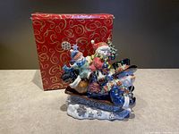 Front and side view of ceramic sledding snowmen music box with festive details and original box in background.