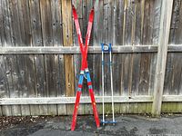 Front view of two red Fischer skis and two blue and white Exel junior ski poles leaning against a wooden fence.