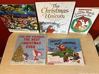 Five children's Christmas books shown together on a red surface, titles visible: The Christmas Story, The Christmas Unicorn, The Crunchy Munchy Christmas Tree, Fox and Squirrel The Best Christmas Ever, Froggy's Best Christmas.
