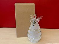 Glass angel LED decoration with original cardboard box on red background.