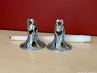 Pair of pewter Iris Seagull candlesticks with one white taper candle laid horizontally behind them, showing full shape and design details.