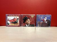 Front view of three Christmas music CDs including Greetings from Santa, Frank Sinatra Ultimate Christmas with cracked jewel case, and Joy to the World Christmas compilation.
