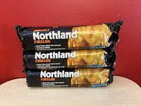 Front view of three sealed Northland Firelogs stacked with the label clearly visible describing burn time and clean burn.