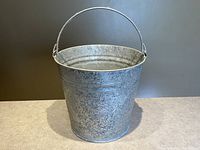 Front view of galvanized metal bucket showing round shape, rim, and attached handle.