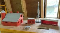 Model train buildings set including barn with silo, outbuilding, windmill, and shed on shelf with window background.