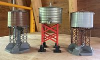 Photo of three cylindrical Lionel Plasticville water towers with metal tanks and painted supports, two grey and one red.