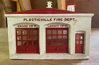 Photo of Plasticville Fire Dept. building with a white textured exterior, red doors labeled Engine Co 7 and Ladder Co 8, red roof, and small side door