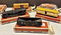 Five Lionel model rail cars displayed with original Lionel boxes. Includes black Lehigh Valley coal car, two black flat freight cars, yellow PRR Baby Ruth box car, Timken roller freight car, and orange Gulf tank car.