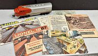 Photo shows two Lionel Santa Fe 2383 F3 AA locomotives along with various vintage Lionel pamphlets including 1957 and 1962 instruction and accessory catalogs, laid out on a table.