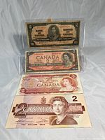 Four Canadian two dollar bills arranged in a row showing front sides, displaying various portraits and designs from 1937 to 1986.