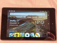 Tablet screen displaying home screen interface with weather and apps visible, showing device is powered and functional.