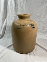 Front view of antique stoneware jug showing beige glaze and faint cobalt blue script on curved body