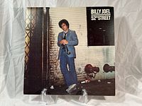 Front cover of Billy Joel 52nd Street album showing Billy Joel holding a trumpet in a blue suit against a brick wall.