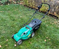Green electric lawn mower with black grass collection bag on lawn, showing left side and front angle.