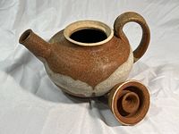 Side view of the brown and beige ceramic teapot body with lid removed, showing open mouth and spout.