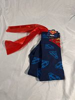 Front view of the folded dark blue knee-high socks with red satin cape, showing Superman logos.