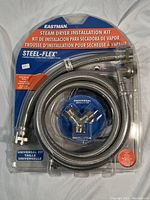 Packaged Eastman Steam Dryer Installation Kit showing braided hoses and universal connector inside clear plastic blister pack