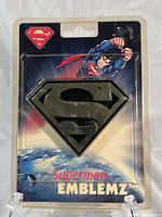 Front view of the Superman car emblem in original blister packaging showing the emblem and Superman illustration.