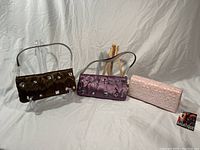 Photo showing the three clutch purses together: copper, lavender, and pink. The copper and lavender purses have zippers, and the pink purse has a floral textured design with a magnetic clasp.