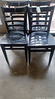 Photo of four black wooden chairs with ladder back design, showing overall condition and grouping of chairs