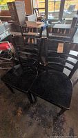 Four black wooden chairs grouped together. Visible scratches and wear on surface. Ladder back design with horizontal slats.