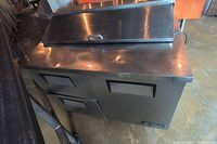 Front view of stainless steel cooler showing two drawers on left, one door on right, and hinged top lid