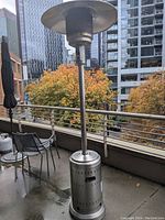 Full view of the tall stainless steel outdoor patio heater on a balcony with city background.