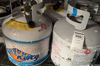 Photo showing two propane tanks side by side, one labeled 'King' with blue graphics, protective collars, valve tops visible.