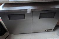 Front view of stainless steel cooler with two hinged doors, black recessed handles and stainless steel top.