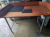 Front view of restaurant sandwich preparation table with reddish-brown work surface, raised edges, and black rubber mats.