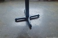 Close-up photo of the black metal base with four legs of the table showing on concrete floor.