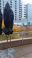 Three closed black umbrellas on wooden poles with round metal bases on balcony