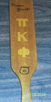 Front side of vintage wooden fraternity paddle displaying name Fraser Grant, gold Greek letters Pi Kappa Phi, black circled number 10 and decorative knot.