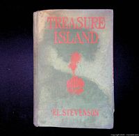 Front cover of vintage "Treasure Island" book showing faded green cloth with orange-red embossed text and palm tree emblem. Shows wear and discoloration.