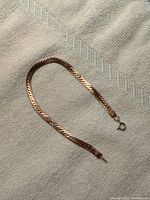 Entire bracelet laid flat on light textile background, showing full length and chain design.