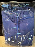 Photo of a folded blue hoodie with the text 'ORRIGINAL LIFE' partially visible through a sealed plastic bag.