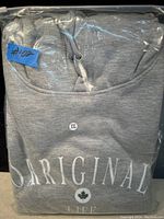 Gray hoodie visible in sealed plastic bag with label #102 and size XXL sticker, showing 'ORIGINAL' text and maple leaf symbol on the fabric.