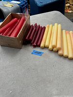 Photo showing candles in red, burgundy, and ivory/yellow colors, some still partially in original packaging.