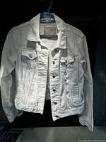 White Banana Republic jean jacket hung on a hanger, showing front button closure, pockets, and classic jean jacket design.