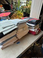 Stack of mostly white and gray towels folded on a table, outdoor setting.