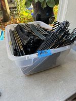 Photo showing a plastic container filled with black plastic model train tracks including straight, curved, and switch types with metal rails.