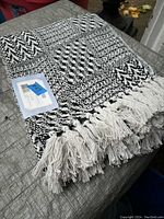 Cotton throw blanket folded to show woven black and white pattern, fringe edges, and original price tag attached.