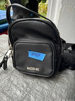 Front view of black small purse with front zip pocket, 'Madden NYC' logo and zipper details.