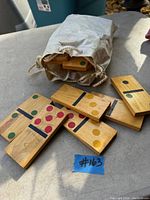Wooden lawn domino tiles displaying colored pips, scattered and next to a canvas storage bag, placed outdoors on a concrete surface.