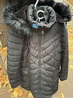Front view of men's black quilted winter coat with fur-trimmed hood, showing material, stitching, and zipper detail